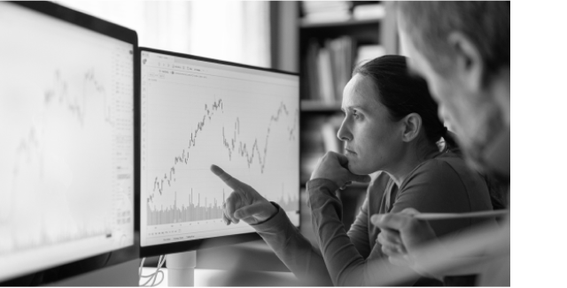 Two people analyzing financial charts on computer monitors.