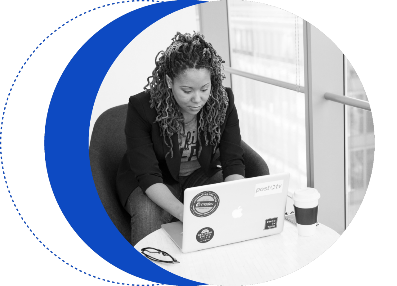 A person with braided hair works on a laptop labeled "Mozilla" and "Post TV" at a table with a coffee cup, in front of a window.
