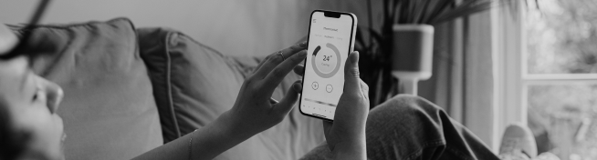 Person adjusting home thermostat through a smartphone app while lying on a couch.