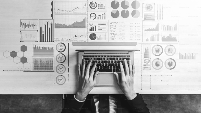 Person typing on a laptop surrounded by various charts and graphs on a desk, depicting data analysis and visualization activities.