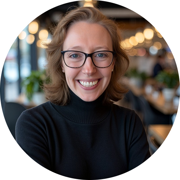 Person wearing glasses and a black turtleneck smiles in a warmly lit indoor setting.